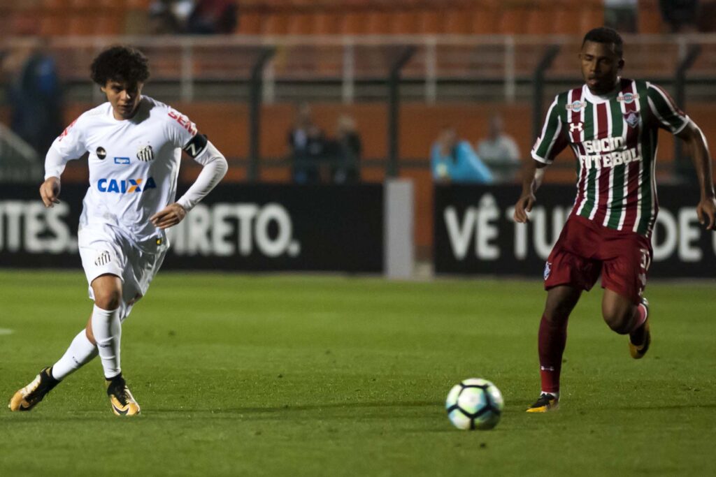 Atleta do Santos e do Fluminense correm em direção a bola durante partida