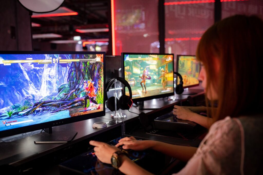 mulher jogando jogos eletrônicos sentada a uma mesa com três monitores
