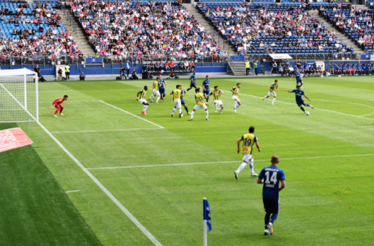 estádio de futebol com jogadores usando uniformes azul e amarelo em campo jogando