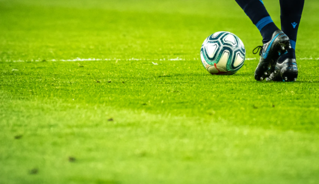 imagem dos pés de jogador em campo com uma bola com detalhes azuis do lado